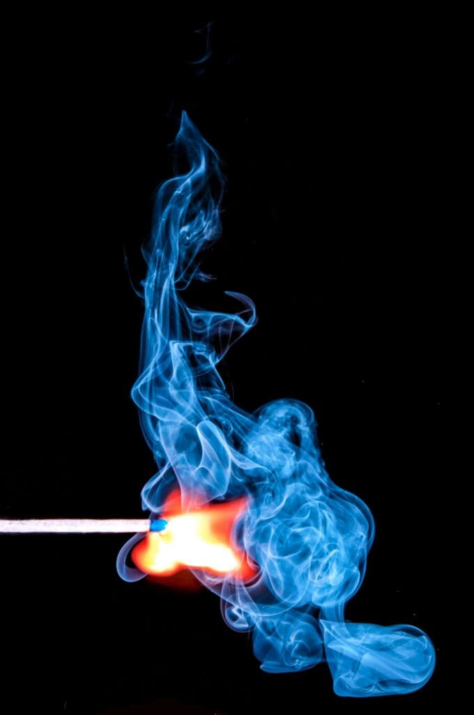 A match ignites with vibrant blue smoke against a black background.