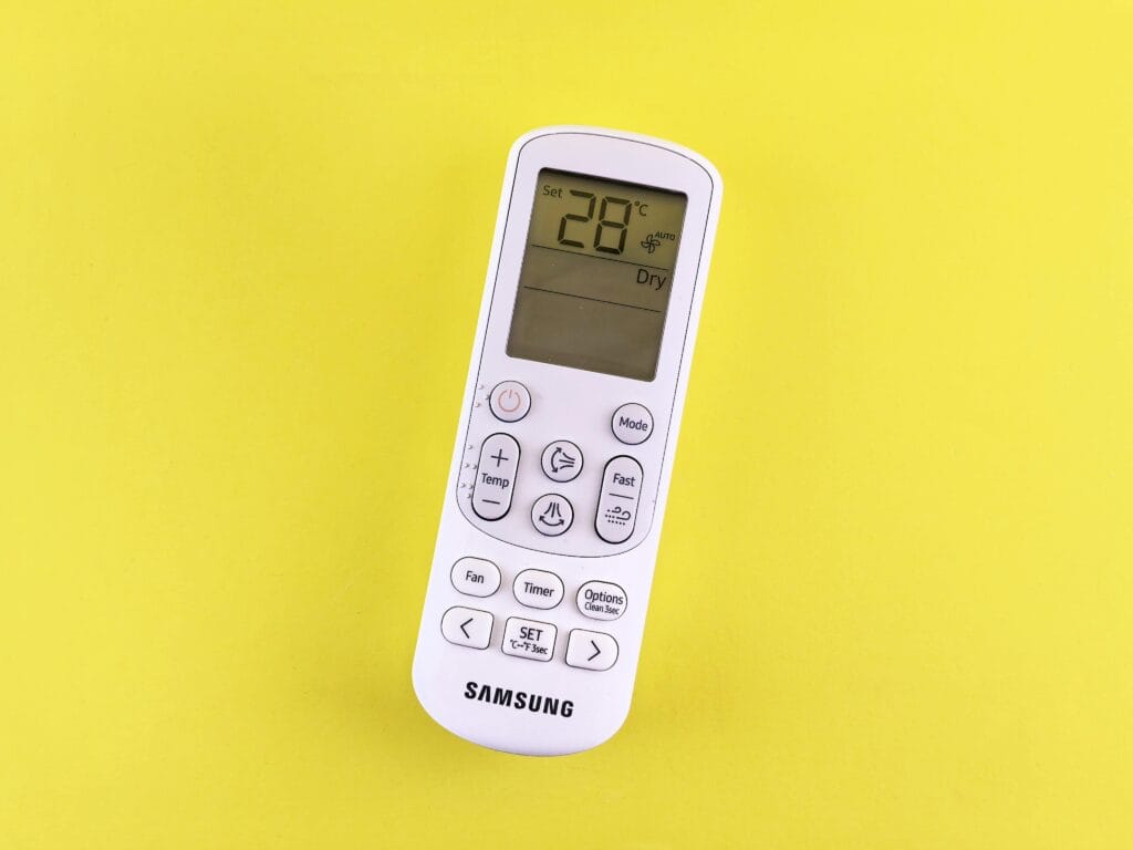 Air conditioner remote with temperature set at 28°C on a yellow background.